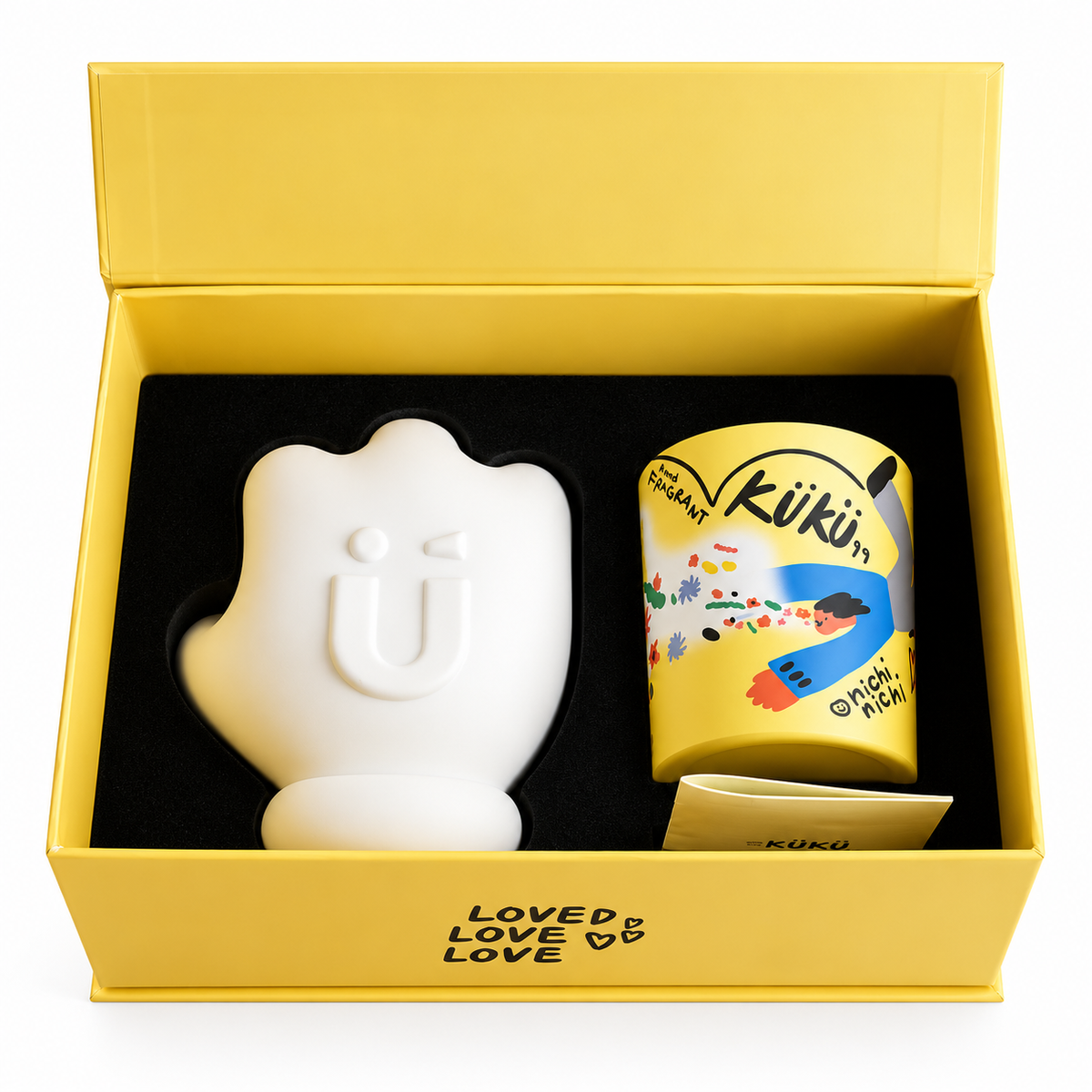 Confezione regalo Speak Kindly aperta, con candela profumata da 200 g nel contenitore giallo illustrato e supporto decorativo bianco a forma di mano.
