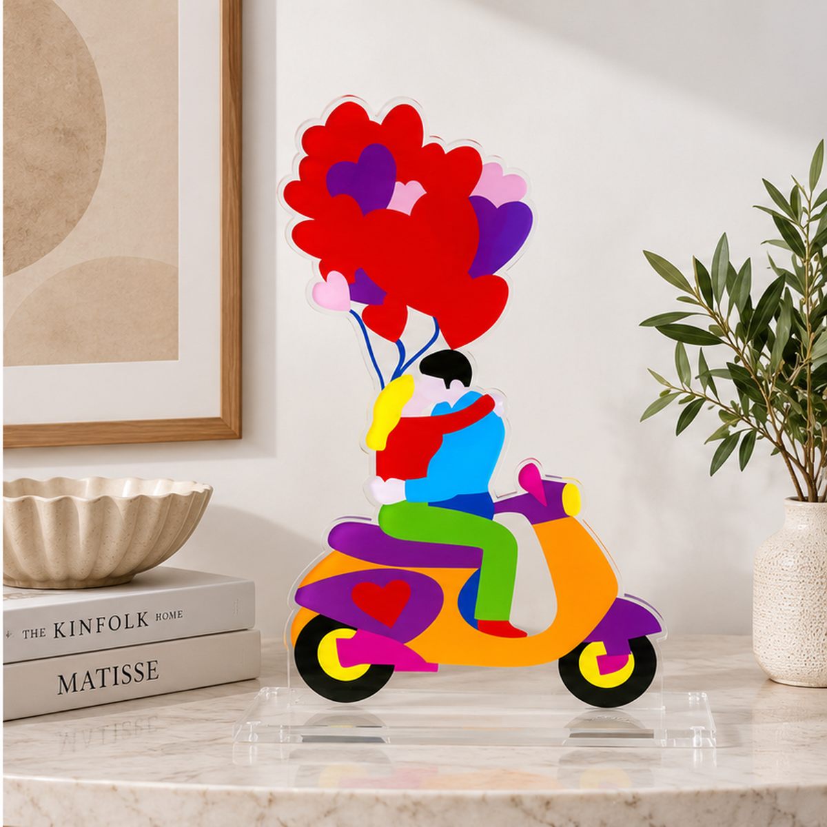 Kiss in Motion di Marco Lodola, scultura colorata con coppia su Vespa e palloncini a cuore, esposta su una consolle in marmo in un ambiente contemporaneo.