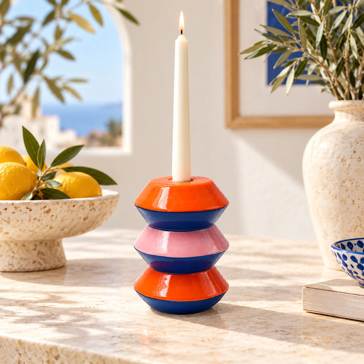 Portacandele Baltasar Qué Rico Amor del Color su consolle in pietra, con candela accesa, agrumi e decorazioni mediterranee.