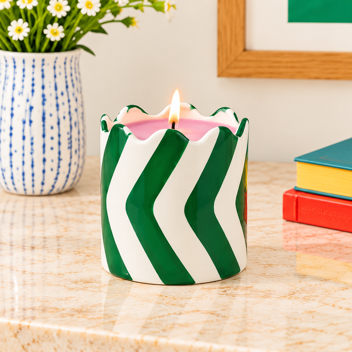 Candela Qué Rico in vaso verde e bianco con bordo ondulato, accesa su un piano in pietra in un ambiente contemporaneo.
