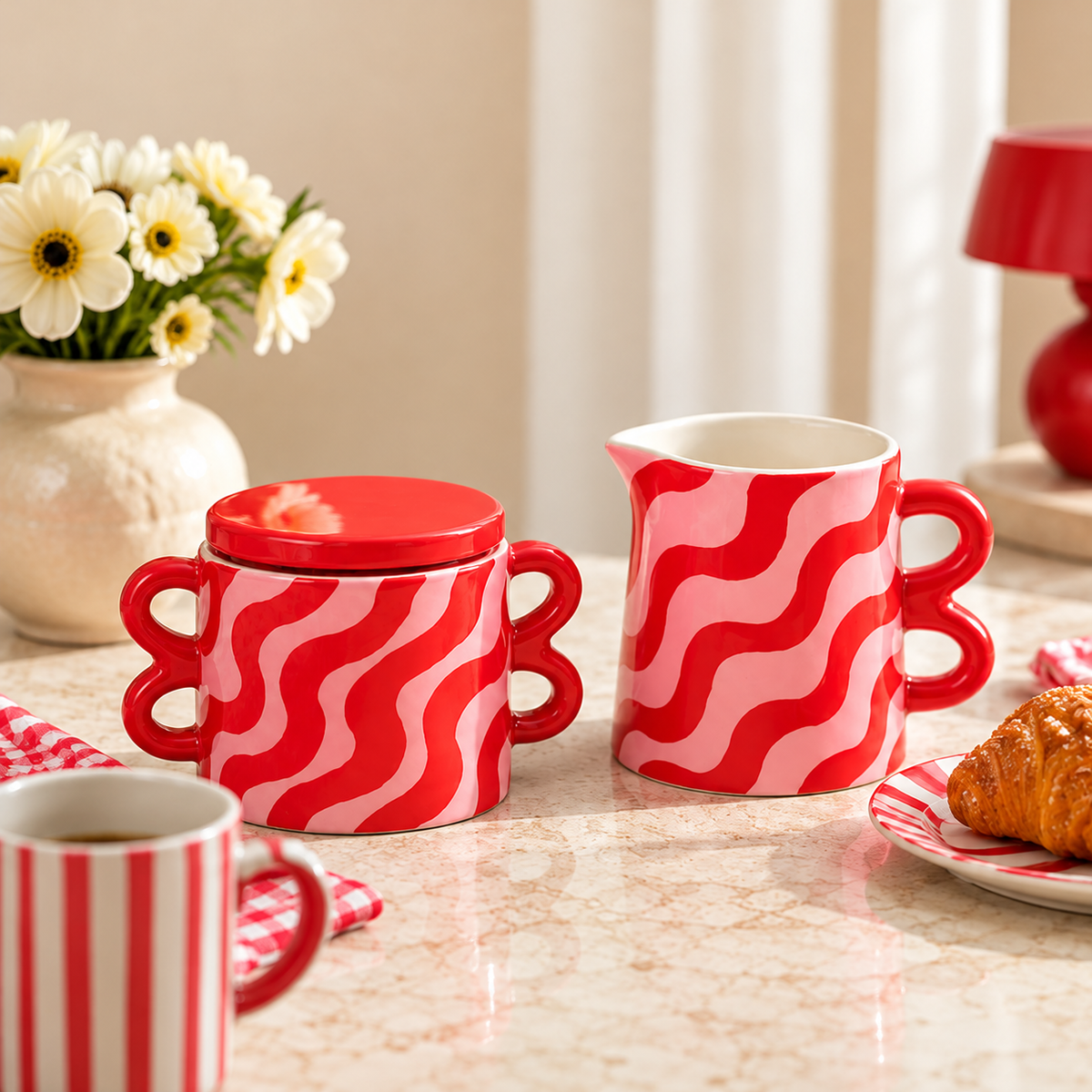 Set in ceramica Que Rico Nata Clarita con zuccheriera e lattiera nei toni rosa e rosso, inserito in un’ambientazione decorativa luminosa e curata.