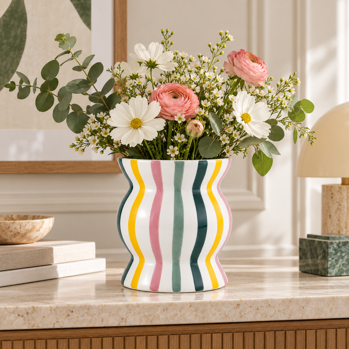 Cachepot Ignacio Qué Rico a righe multicolore con fiori rosa, bianchi e gialli, ambientato su una consolle in pietra chiara.