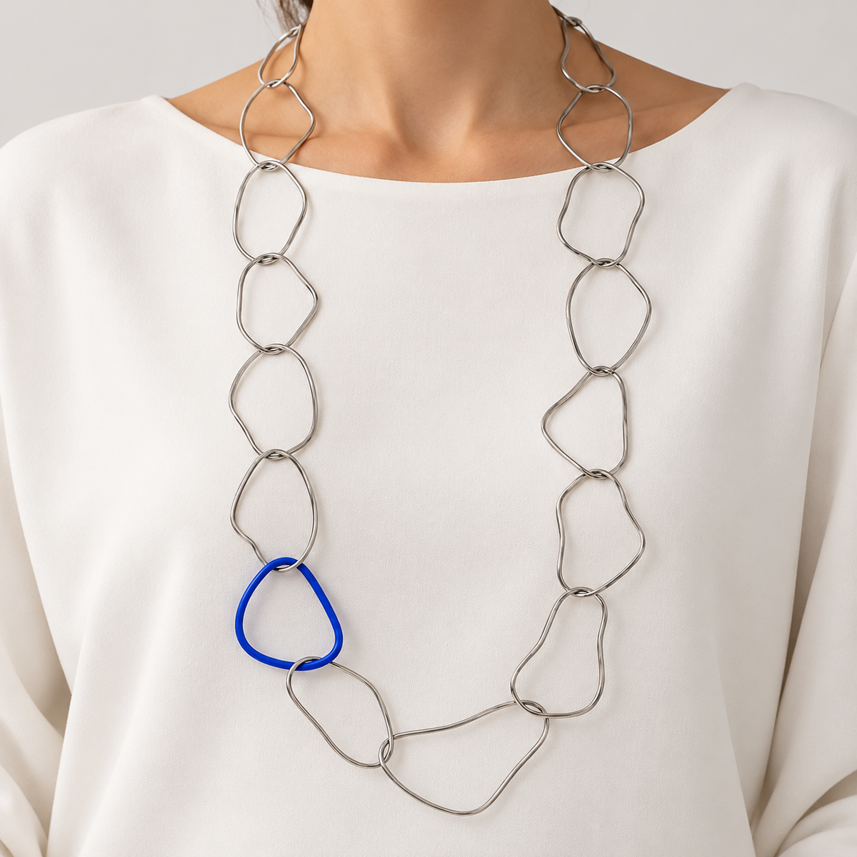 Collana Memory+ in acciaio argentato con dettaglio blu cobalto, indossata su un abito bianco, con anelli lunghi e irregolari.