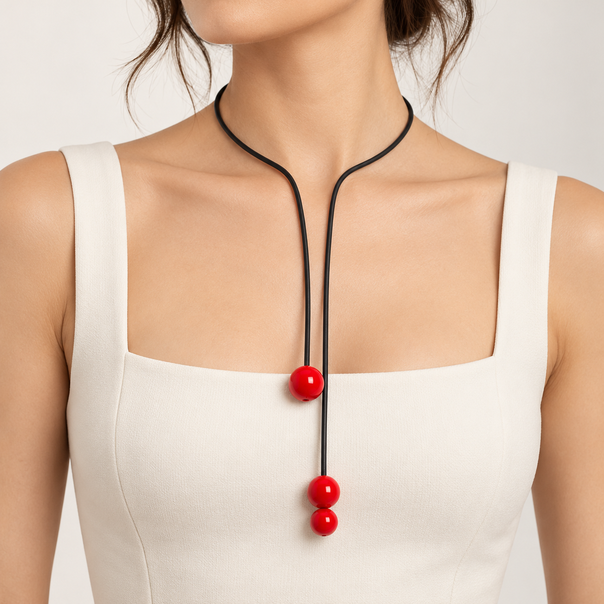 Collana Play Lunga in caucciù nero con tre sfere rosse lucide, indossata con abito bianco in stile contemporaneo.