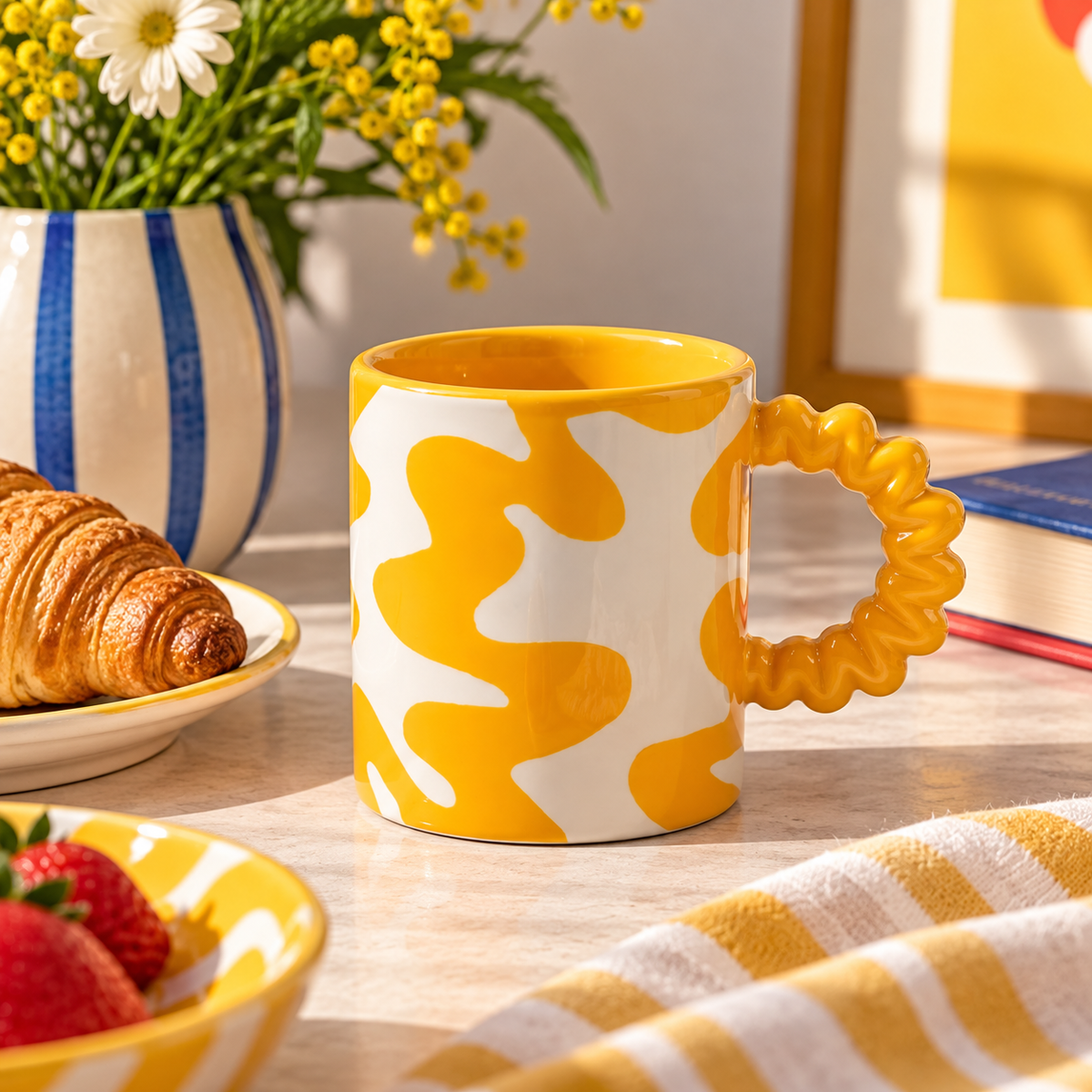 Mug Daniela Qué Rico in ceramica bianca e gialla con manico ondulato, ambientata su un tavolo per la colazione con croissant e fiori.