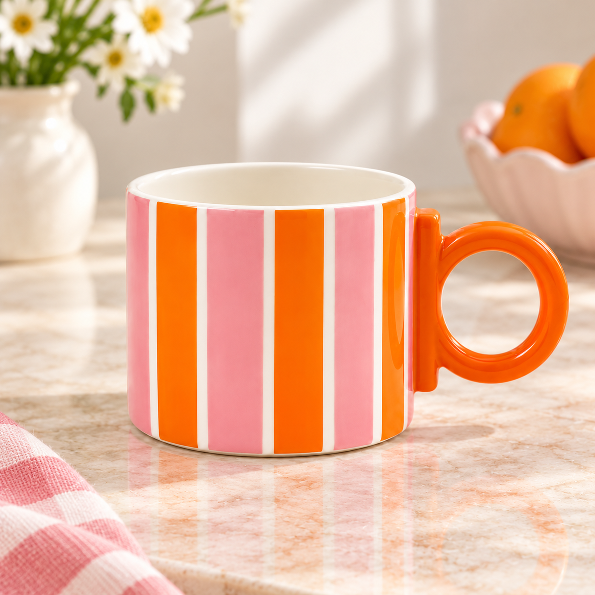 Mug Inés Qué Rico in ceramica a righe verticali rosa e arancioni, con manico circolare arancione, ambientata su un piano in marmo chiaro.