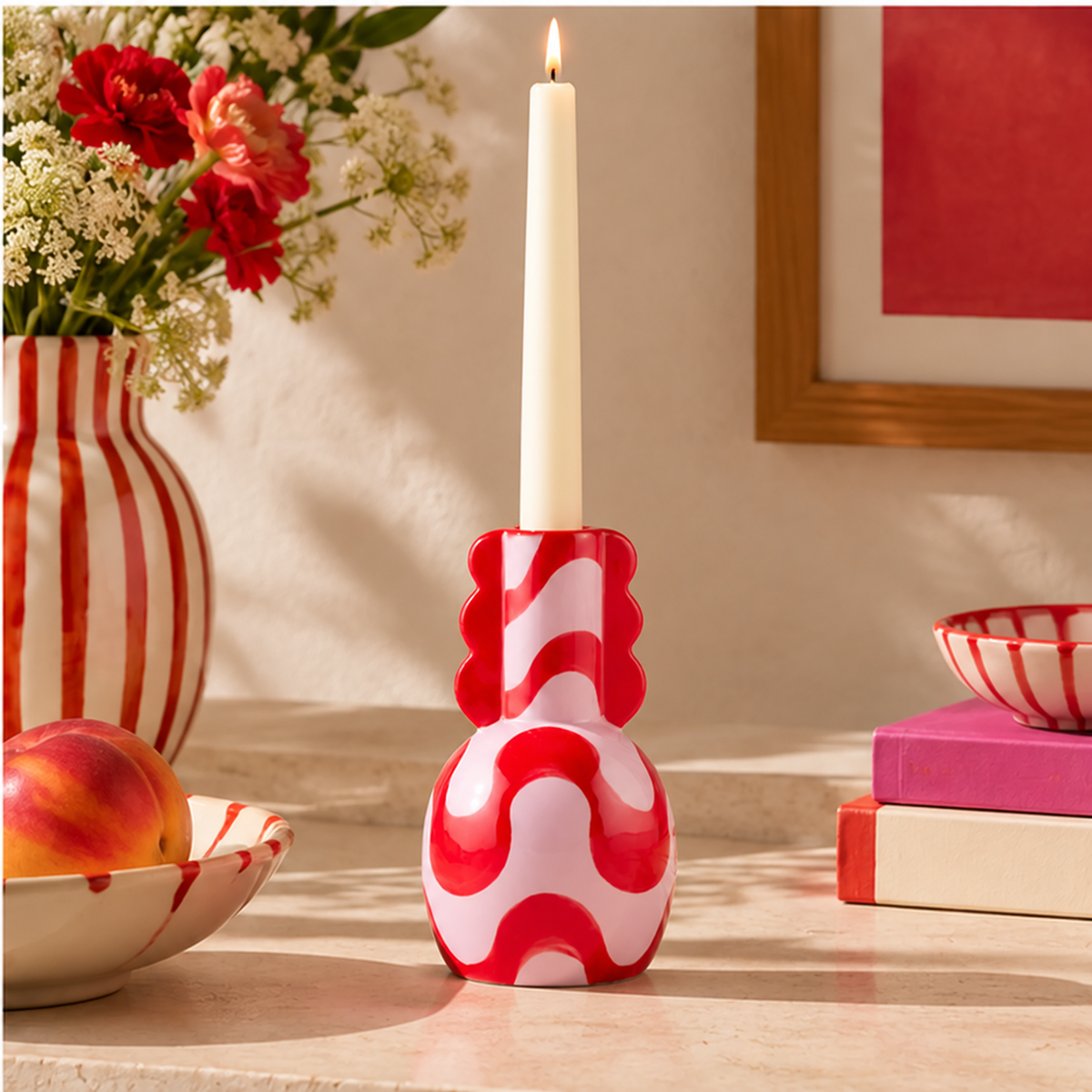 Portacandele Adelina Qué Rico rosa e rosso con candela accesa, su una consolle chiara con fiori e ceramiche decorative.