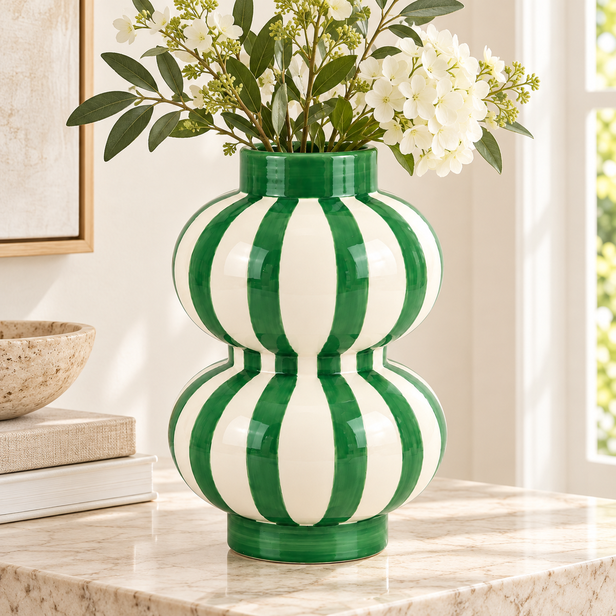 Vaso Augusto Rayas Bailarinas Qué Rico verde e bianco con fiori bianchi e rami verdi, ambientato su una consolle in pietra chiara.