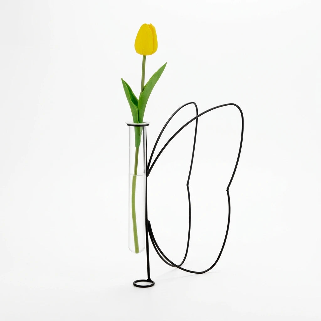 Vaso Butterfly Silhouette Balvi con struttura a farfalla in metallo nero, provetta trasparente e tulipano giallo, su fondo bianco.