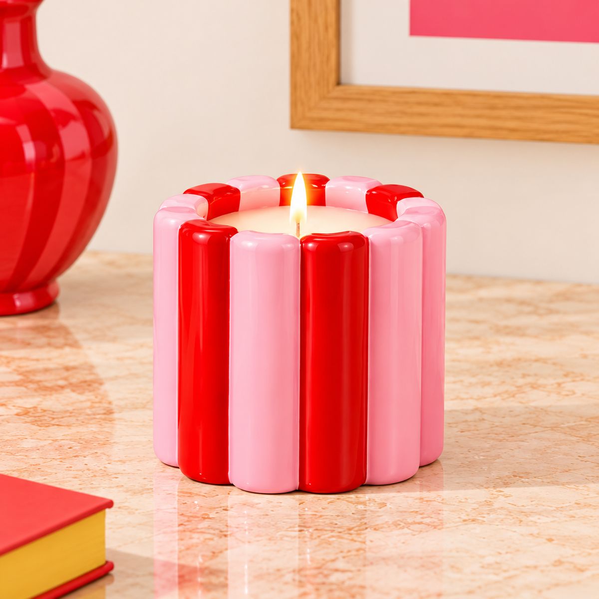 Candela Qué Rico in vaso di ceramica rosso e rosa a righe verticali, accesa su un tavolino in un interno luminoso.