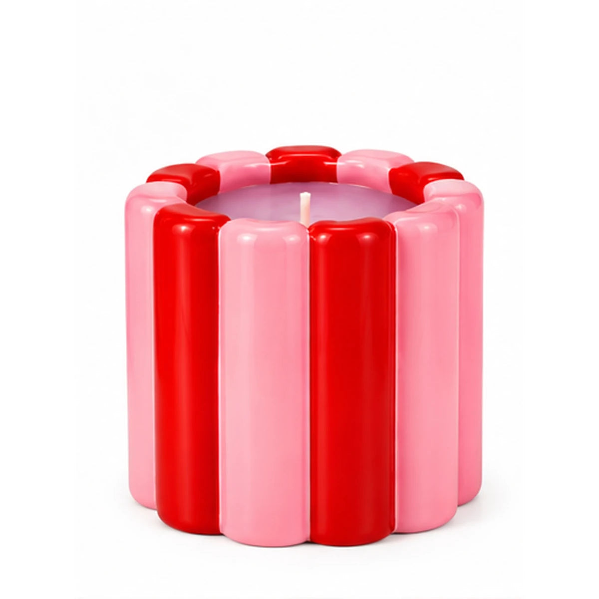 Candela Qué Rico in vaso ad anelli bianchi, rosa e rossi, accesa su un mobile con fiori e complementi decorativi.