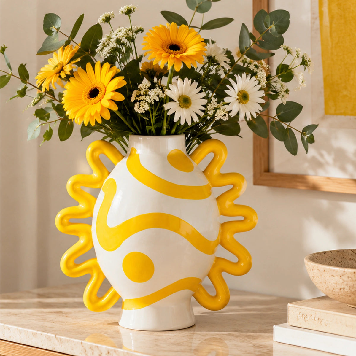 Vaso Isabel Sol y Sombra Qué Rico bianco e giallo con fiori gialli e bianchi, ambientato su una consolle in pietra chiara.