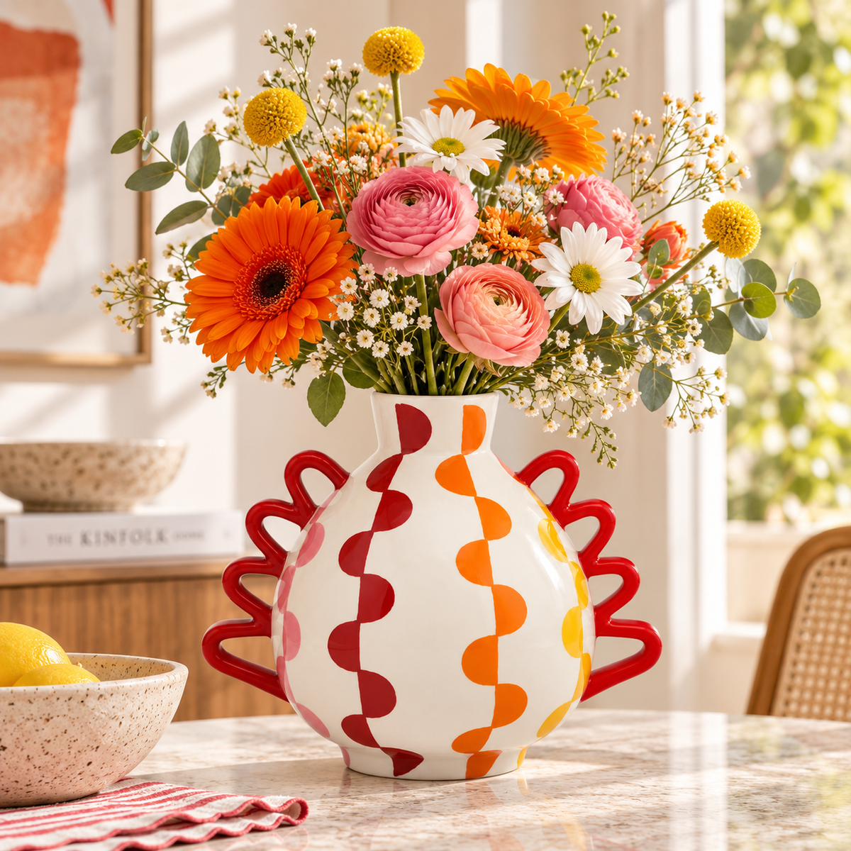 Vaso Manolo Groovy Grids Qué Rico con manici rossi e bouquet di fiori arancioni, rosa e bianchi, ambientato su una superficie in pietra chiara.