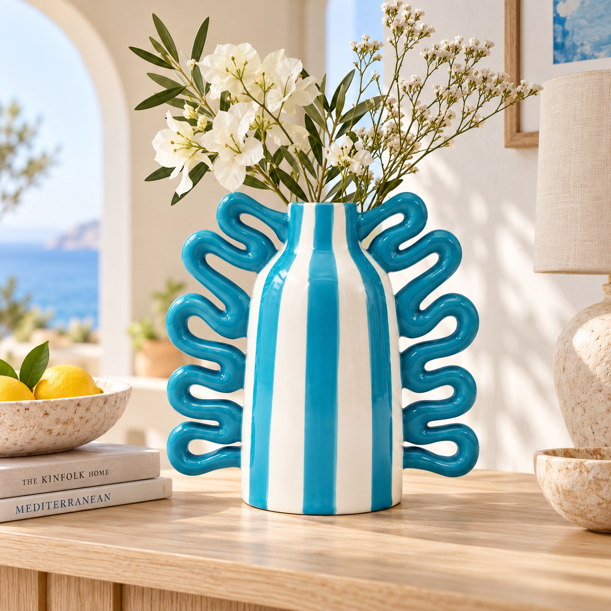 Vaso Nicolás Rayas Bailarinas di Qué Rico in ceramica bianca e azzurra con manici ondulati, ambientato su una consolle con fiori bianchi.